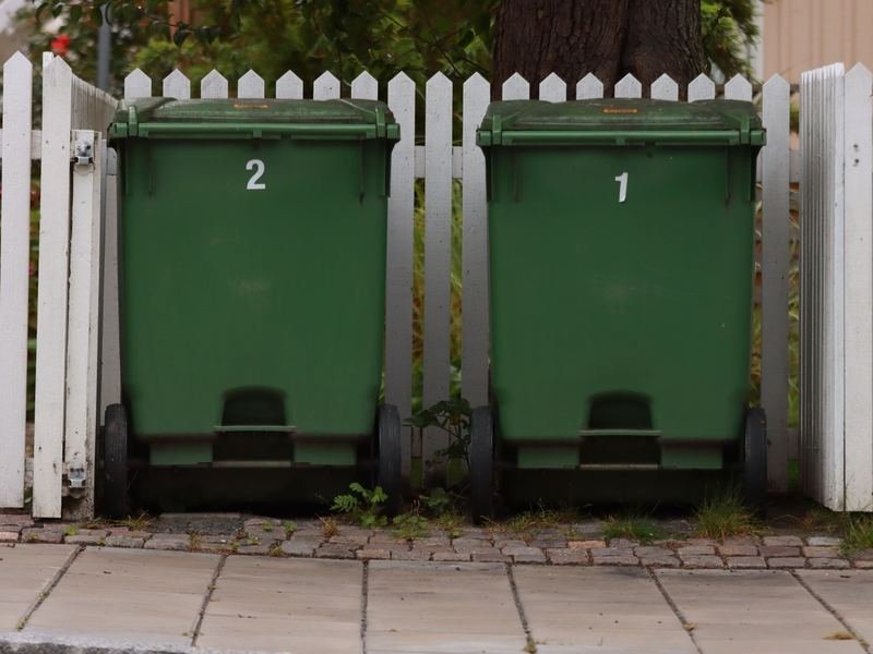 Two green wheelie bins beside a white fence